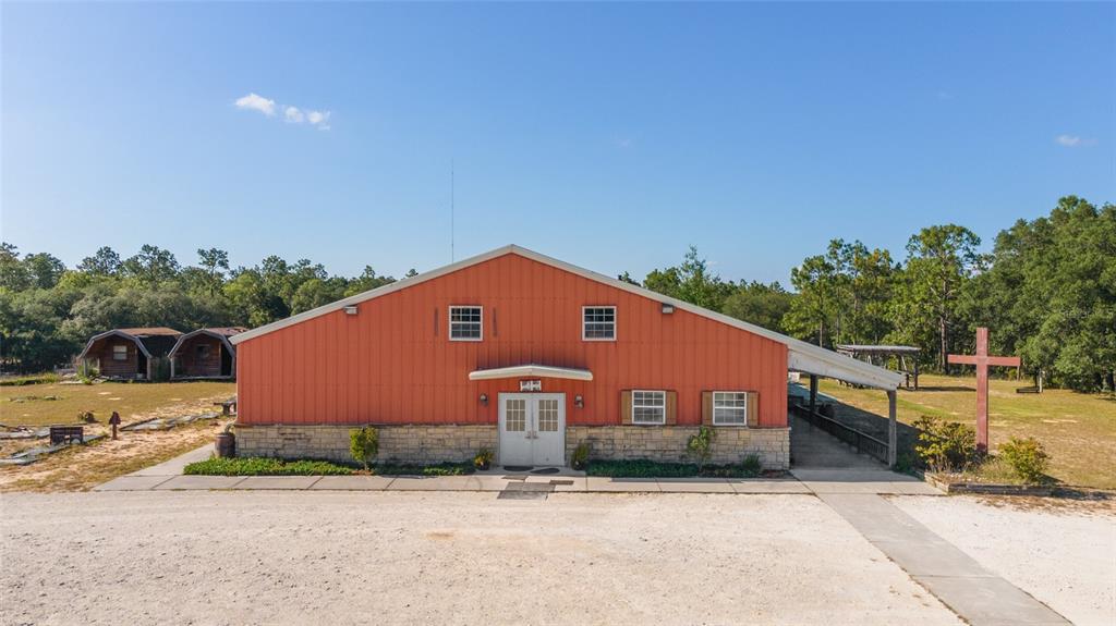 A red metal-sided building with a stone base and a large wooden cross outside — 6491 & 6481 SE 123RD TERRACE, MORRISTON, FL