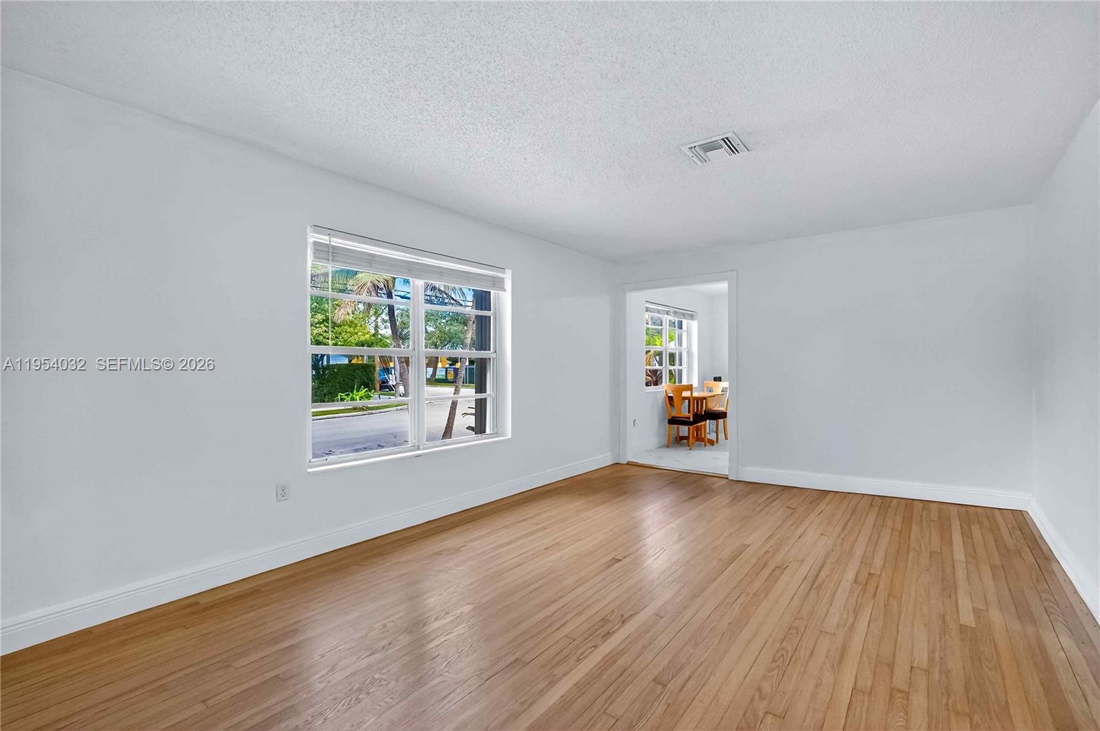 An empty room with white walls, hardwood floors, and a view into an adjacent dining area — 2399 SW 26th Ln, Miami FL 33133, MIAMI, FL