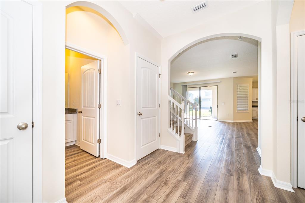 A bright entryway features wood-look flooring, arched doorways, white doors, and a staircase leading upstairs — 9463 KOMIKA LANE, WINTER GARDEN, FL