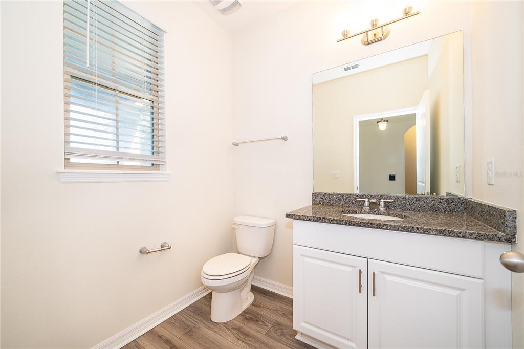 A bathroom features a white vanity with a granite countertop, a toilet, and wood-look flooring — 9463 KOMIKA LANE, WINTER GARDEN, FL