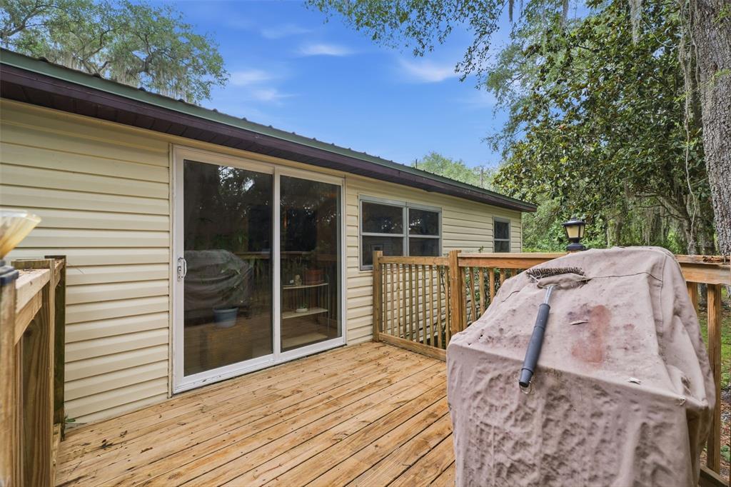 A wooden deck with a covered grill sits outside a house with light-colored siding — 7663 CR 247, LAKE PANASOFFKEE, FL