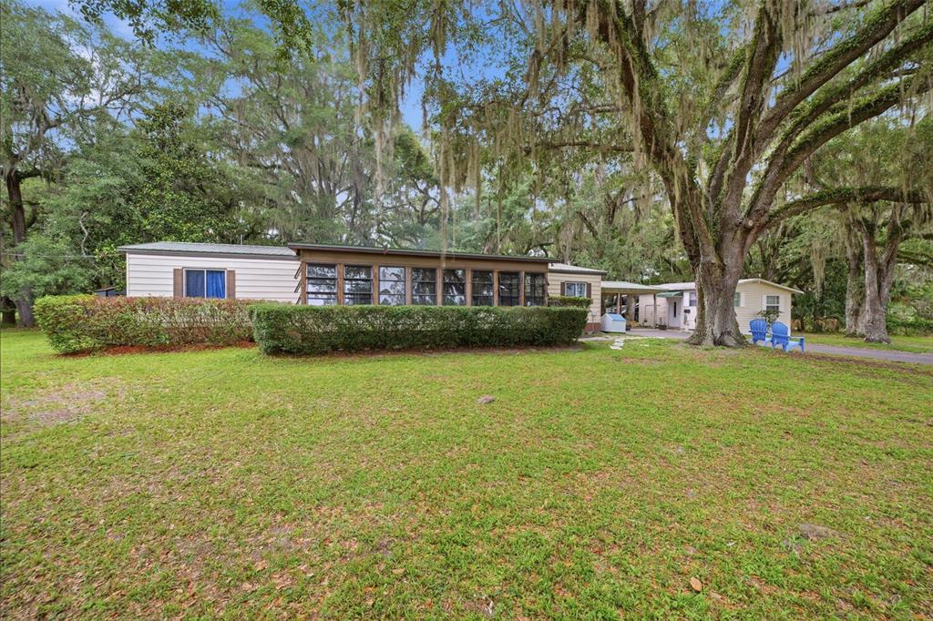 A single-story house with a screened-in porch sits on a grassy lot under large trees — 7663 CR 247, LAKE PANASOFFKEE, FL
