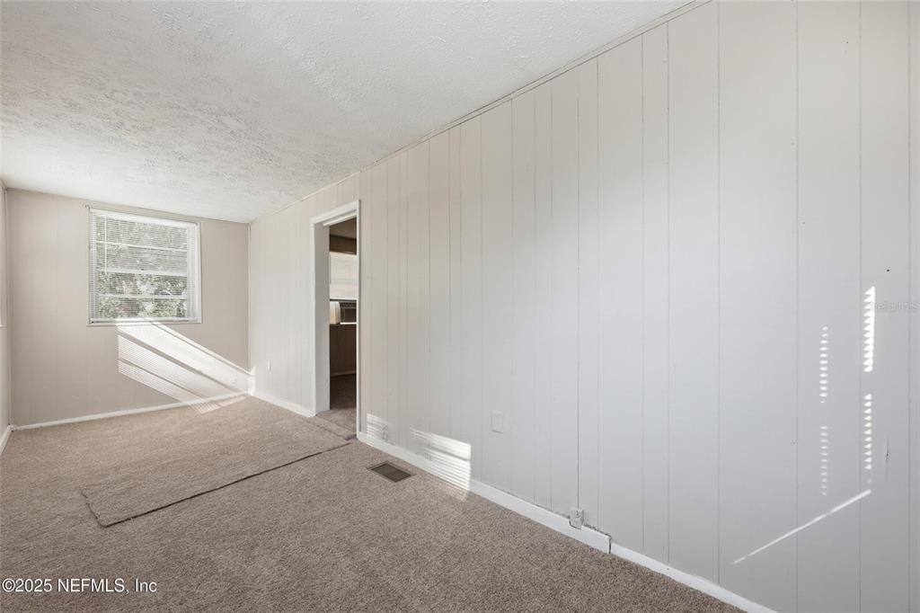 An empty room features beige carpeting, light-colored wood paneling, and a single window — 1217 W 29TH STREET, JACKSONVILLE, FL