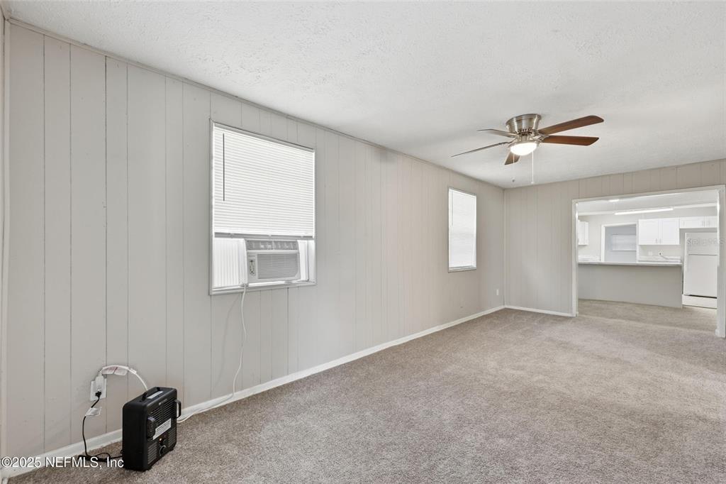 A living room features light gray paneled walls, beige carpeting, a ceiling fan, and a window unit — 1217 W 29TH STREET, JACKSONVILLE, FL