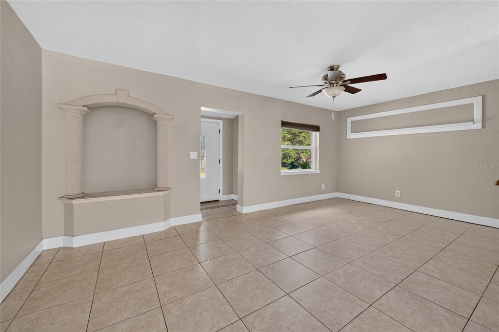 A living room features beige walls, tile flooring, a decorative arched alcove, and a ceiling fan — 1145 GEORGE ANDERSON STREET, ORMOND BEACH, FL