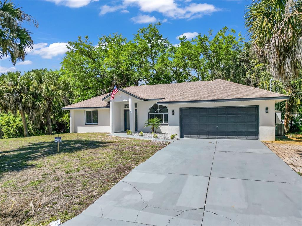 A single-story house with a gray garage door, white exterior, and a paved driveway — 26140 HAPSBURG ROAD, PUNTA GORDA, FL