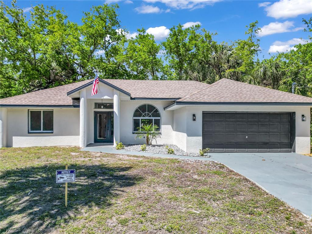 A single-story house with white stucco walls, a dark garage door, and a front entrance — 26140 HAPSBURG ROAD, PUNTA GORDA, FL