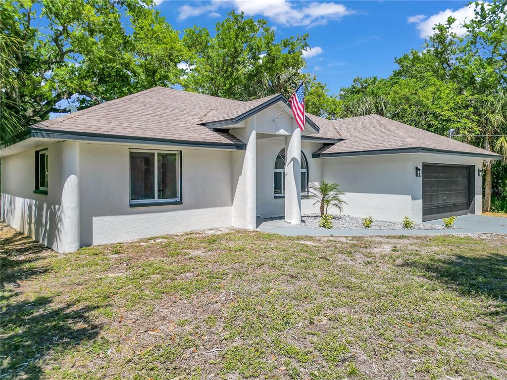 A single-story white house with a dark roof, garage, and an American flag out front — 26140 HAPSBURG ROAD, PUNTA GORDA, FL
