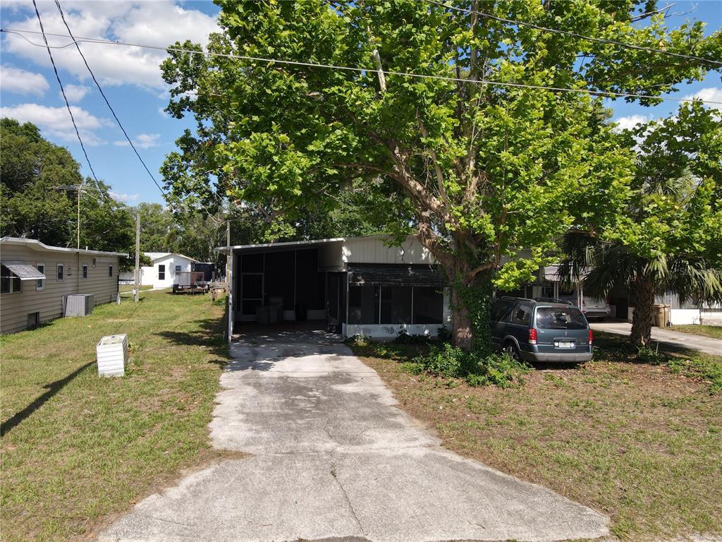A single-story mobile home with a carport and a large tree in the front yard — 28814 HUBBARD STREET, LEESBURG, FL