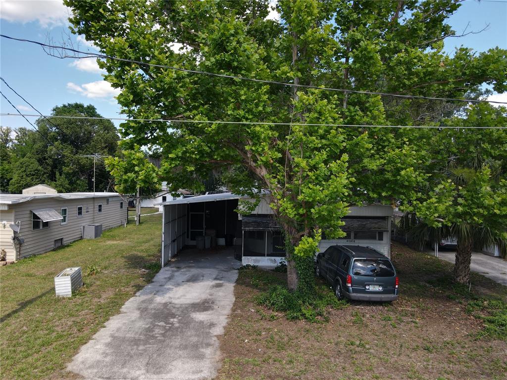An exterior view of a mobile home with a carport, driveway, and large shade tree — 28814 HUBBARD STREET, LEESBURG, FL