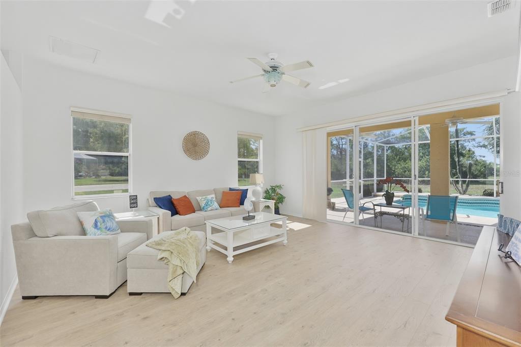 A bright living room features light wood-look flooring, a ceiling fan, and sliding glass doors — 2224 PLATINUM DRIVE, SUN CITY CENTER, FL