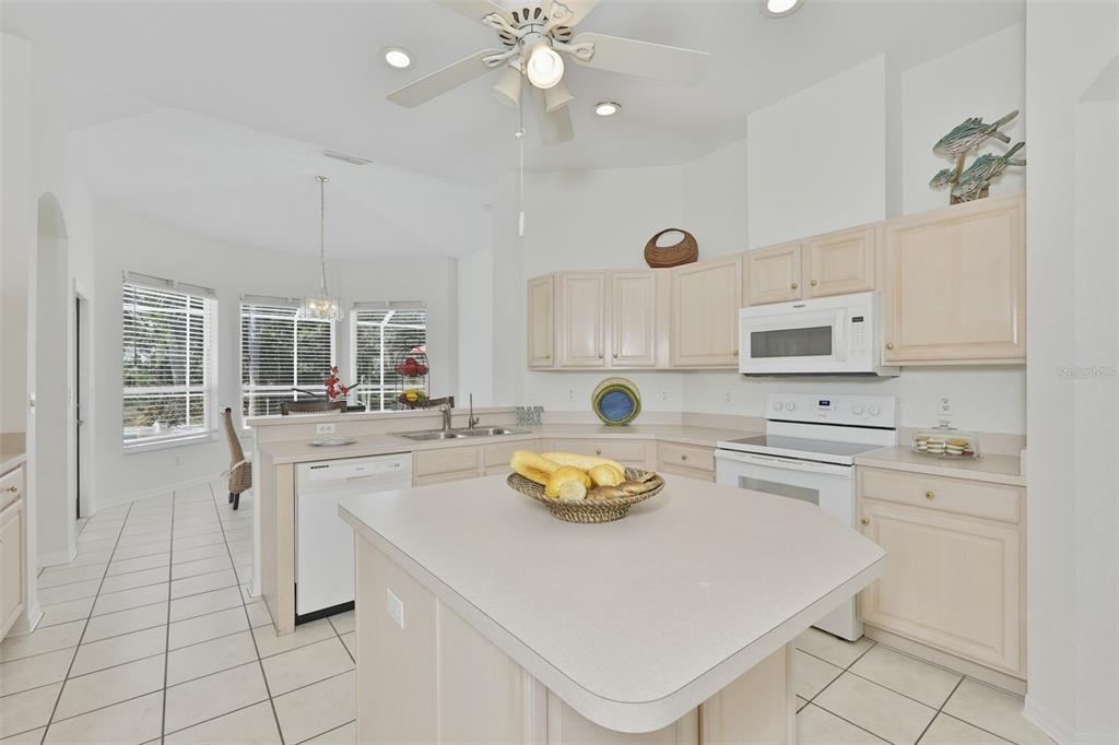 A kitchen features light wood cabinets, a central island, white appliances, and tiled flooring — 2224 PLATINUM DRIVE, SUN CITY CENTER, FL
