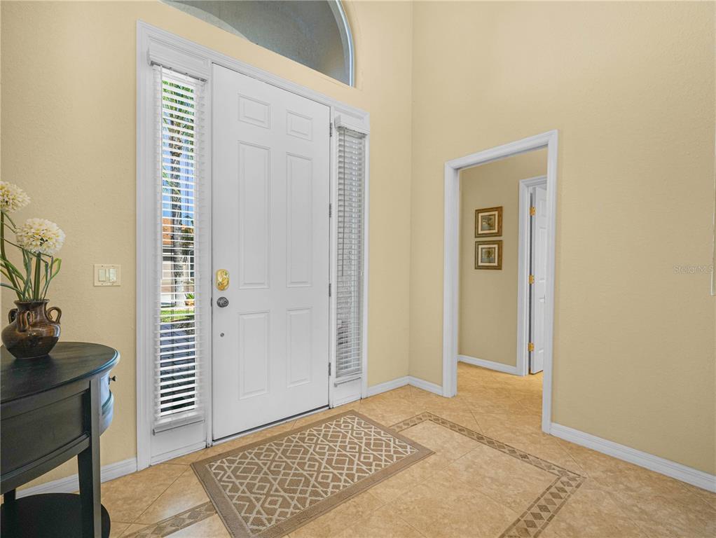 A bright entryway features a white front door, sidelight windows, and light-colored tile flooring — 5337 HOGAN LANE, WINTER HAVEN, FL