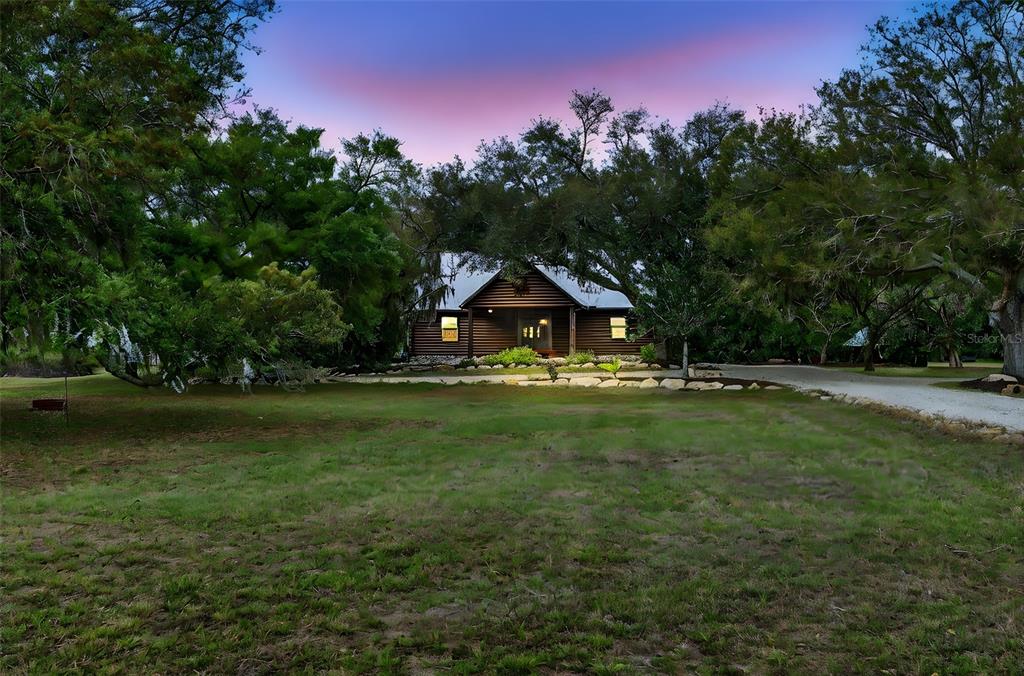 A log cabin house sits nestled among large trees at the end of a driveway — 6888 MYAKKA VALLEY TRL, SARASOTA, FL