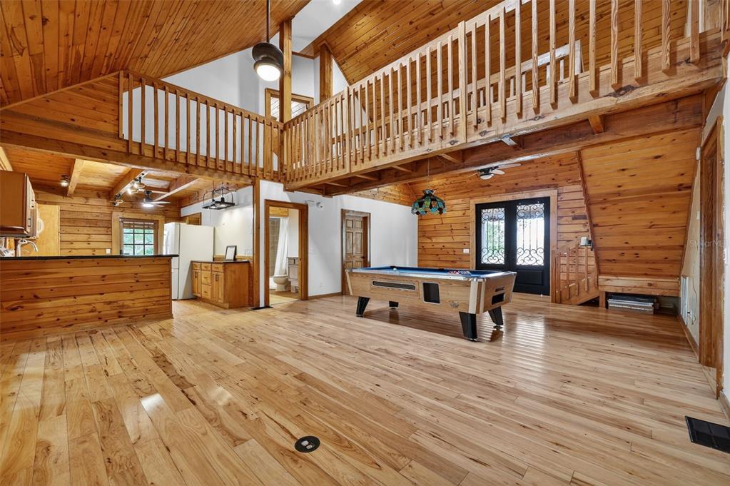 A rustic living area with wood walls, hardwood floors, a pool table, and a loft balcony — 6888 MYAKKA VALLEY TRL, SARASOTA, FL