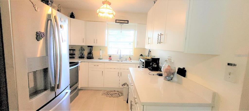 A kitchen features white cabinets, light countertops, stainless steel appliances, and a hanging pendant light — 9 VILLA VILLAR COURT UNIT N/A, DELAND, FL