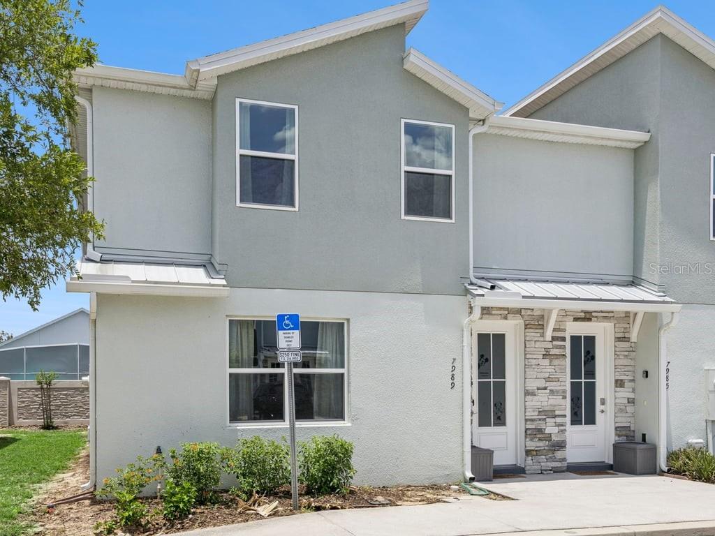 A two-story townhouse exterior features light gray stucco, stone accents, and a handicap parking sign — 7989 FORMOSA VALLEY PLACE, KISSIMMEE, FL