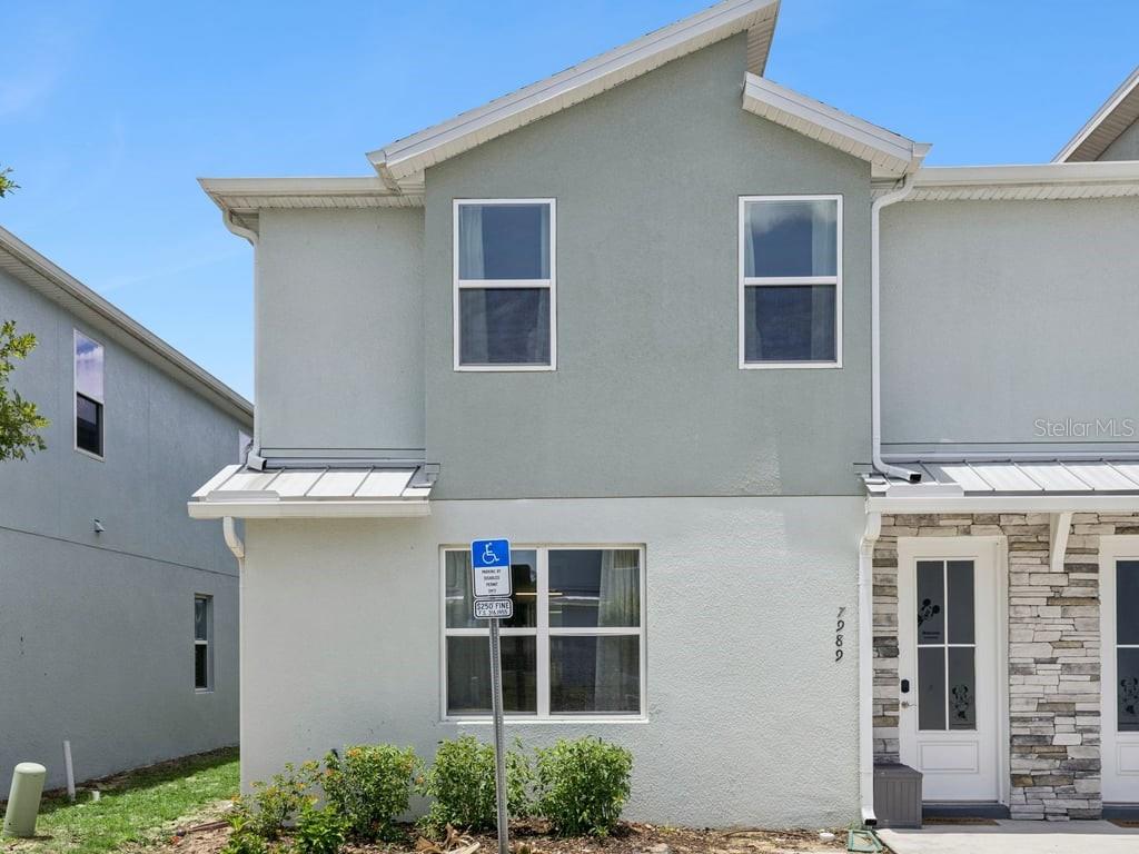 A two-story townhouse exterior features light-colored stucco, a stone-accented entryway, and a handicap parking sign — 7989 FORMOSA VALLEY PLACE, KISSIMMEE, FL
