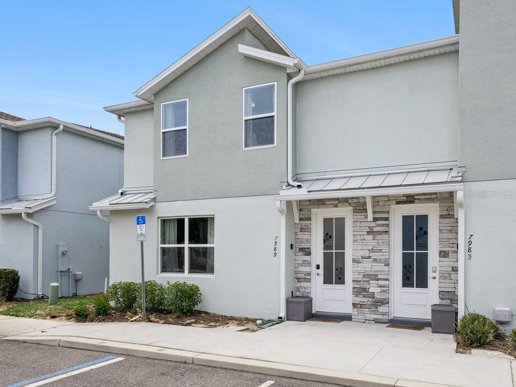 A two-story townhouse exterior features light-colored stucco, stone accents, and two white front doors — 7989 FORMOSA VALLEY PLACE, KISSIMMEE, FL
