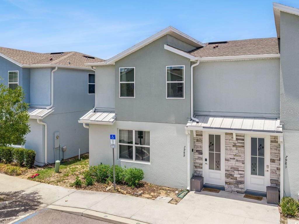 A two-story townhouse exterior features light-colored stucco, stone accents, and two front entry doors — 7989 FORMOSA VALLEY PLACE, KISSIMMEE, FL