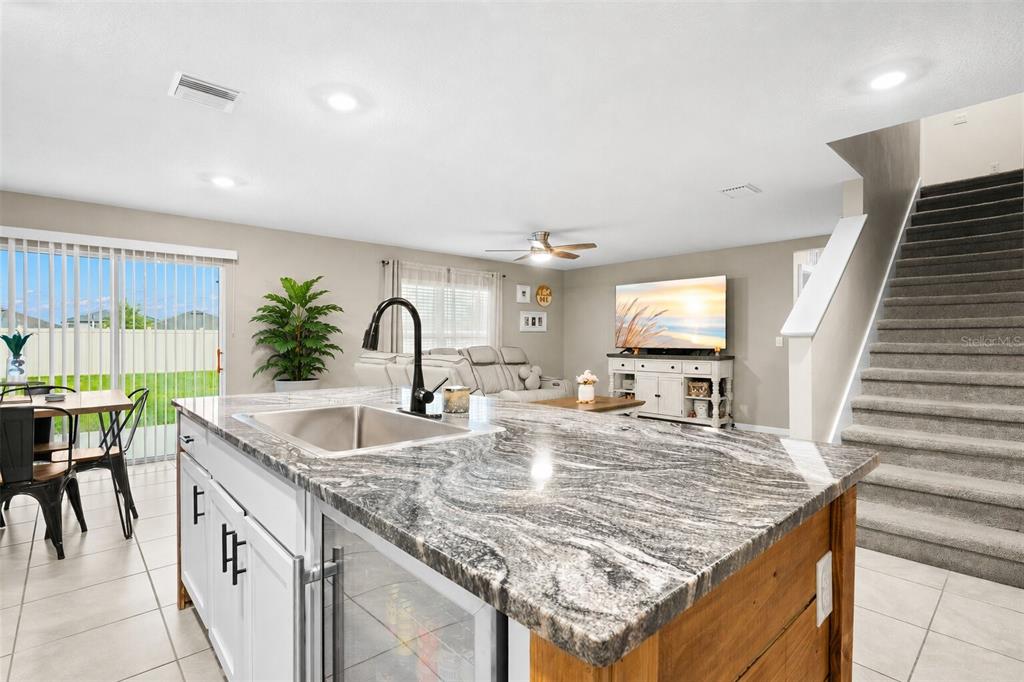 A kitchen island with a granite countertop sits in front of a living area and stairs — 5480 FLINT HILLS DRIVE, WIMAUMA, FL