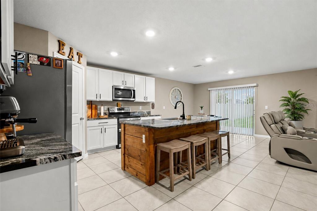 A kitchen features white cabinets, a dark wood island with bar stools, and tile flooring — 5480 FLINT HILLS DRIVE, WIMAUMA, FL