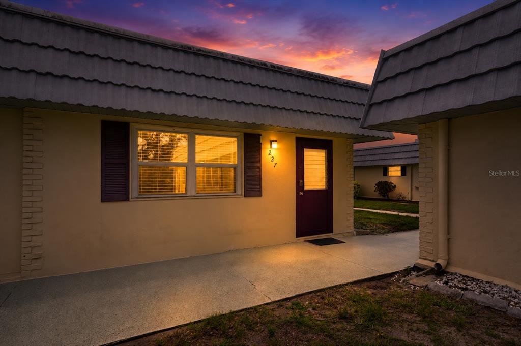 A single-story residential building exterior features a tan facade, dark shutters, and a purple door — 1801 BEDFORD TERRACE UNIT 227, SUN CITY CENTER, FL