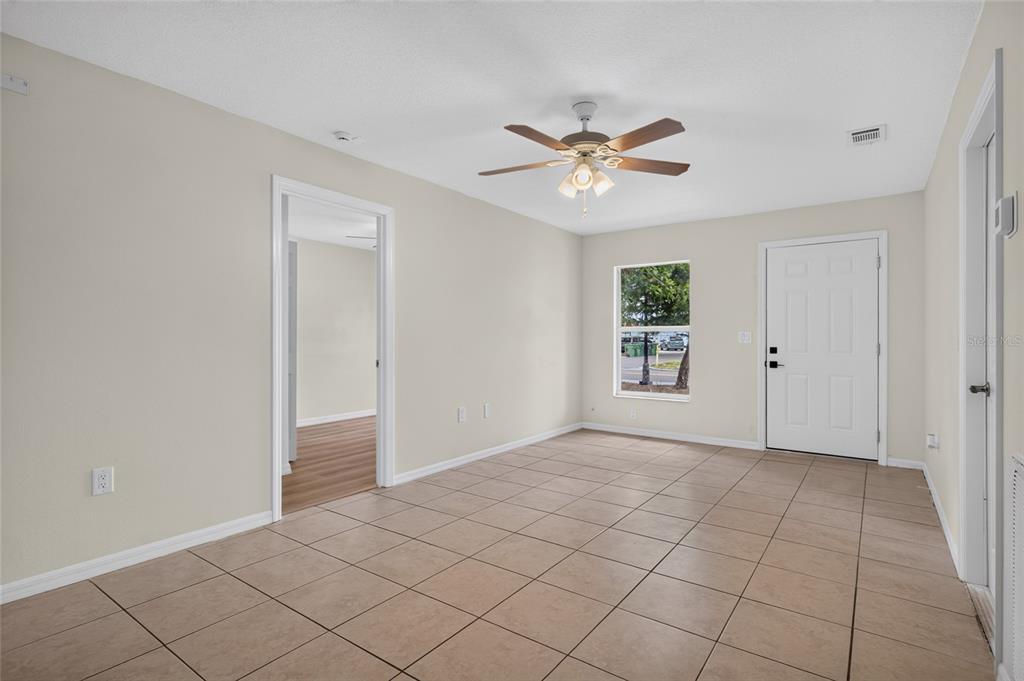 An empty room with beige walls, tile flooring, a ceiling fan, and a white door — 1004 17TH AVENUE W, BRADENTON, FL