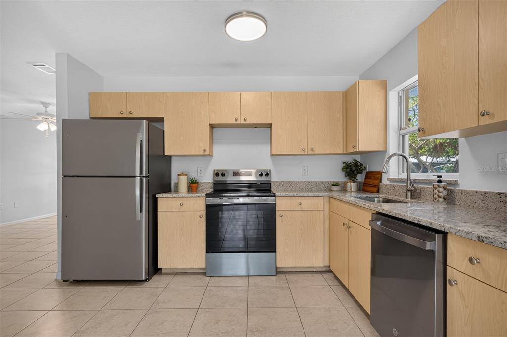 A kitchen features light wood cabinets, granite countertops, and stainless steel appliances on a tiled floor — 1004 17TH AVENUE W, BRADENTON, FL