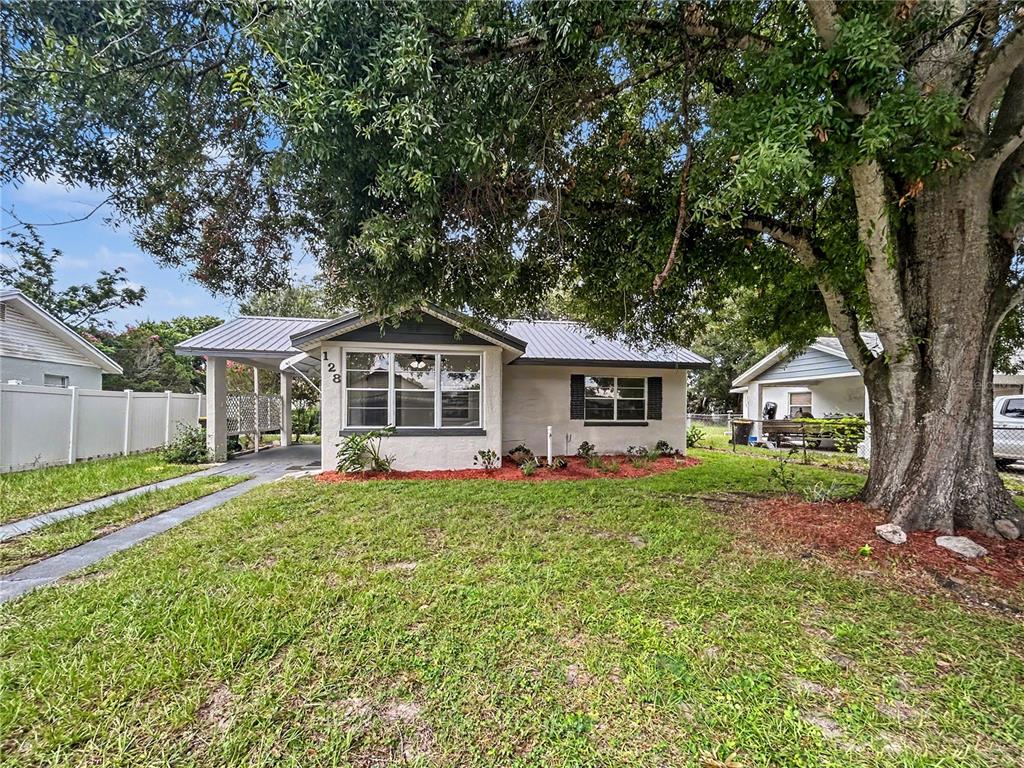 A single-story house with a metal roof, carport, and large tree in the front yard — 128 CENTER STREET, WINTER HAVEN, FL