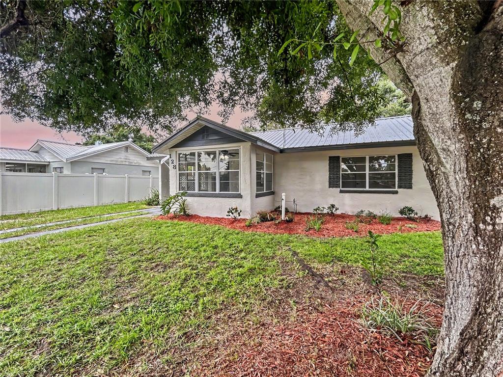 A single-story house with a metal roof, white stucco exterior, and a large front tree — 128 CENTER STREET, WINTER HAVEN, FL