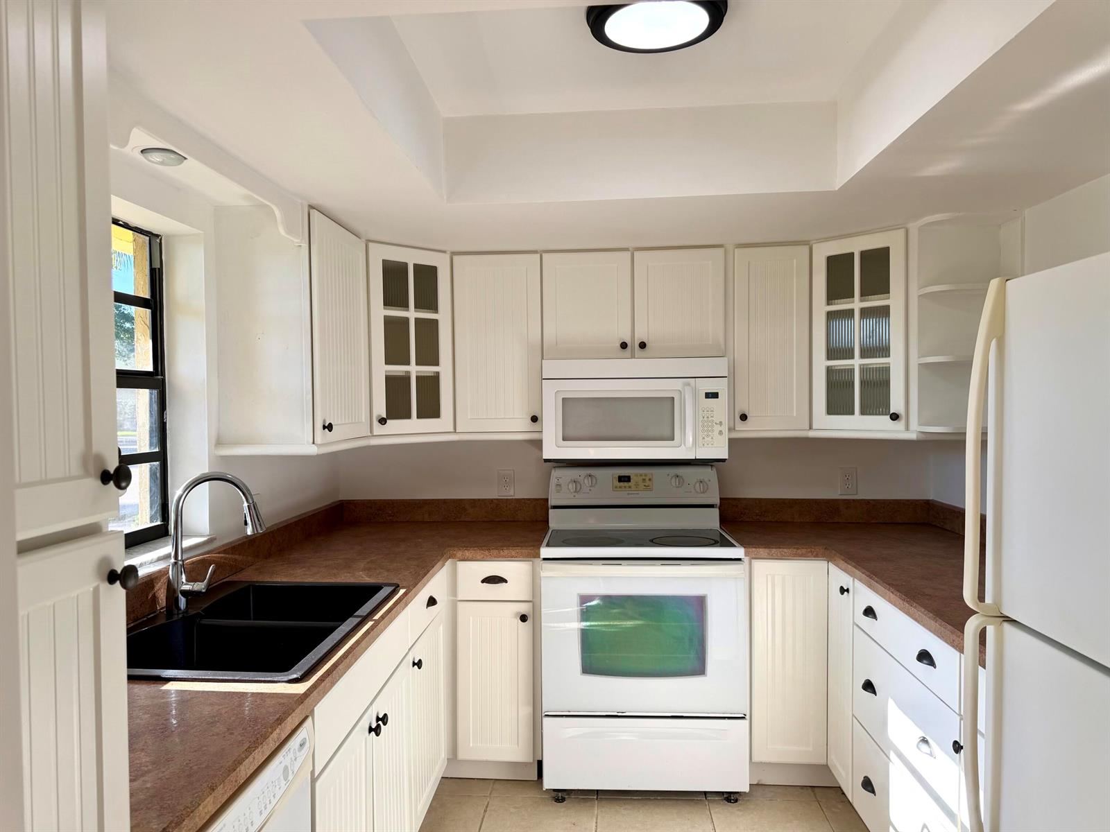 A kitchen with white beadboard cabinets, dark countertops, a black sink, and white appliances — 400 18th Street # B4, Vero Beach FL 32960, VERO BEACH, FL