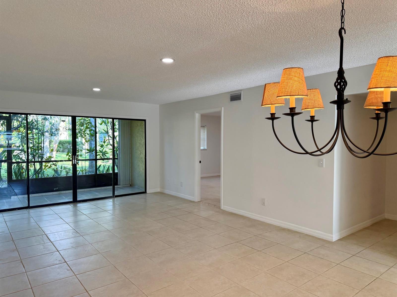 An empty room with beige tile flooring, a chandelier, and sliding glass doors to a patio — 400 18th Street # B4, Vero Beach FL 32960, VERO BEACH, FL