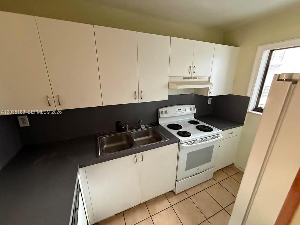 A kitchen features white cabinets, dark countertops, a double sink, and a white electric stove — 6055 W 19th Ave # 305, Hialeah FL 33012, HIALEAH, FL