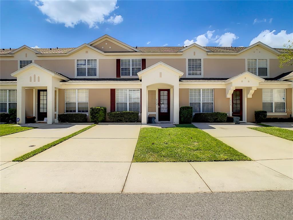A row of townhouses with beige stucco exteriors, white trim, and individual concrete driveways — 2356 SILVER PALM DRIVE, KISSIMMEE, FL