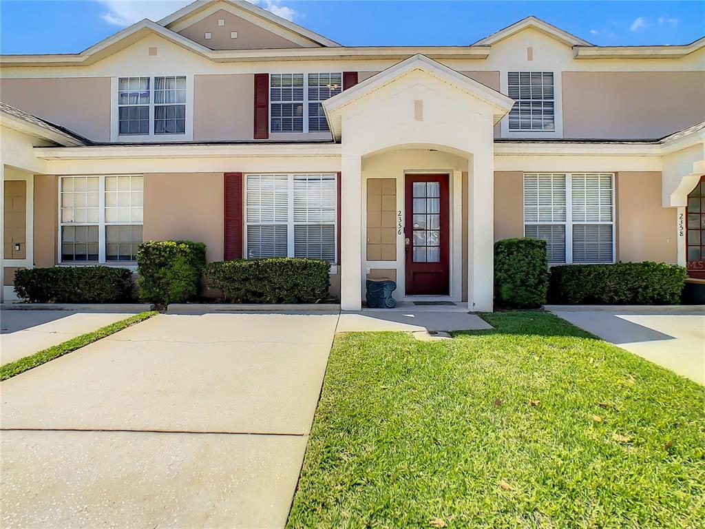 A two-story townhouse exterior features a red front door, beige siding, and a concrete driveway — 2356 SILVER PALM DRIVE, KISSIMMEE, FL