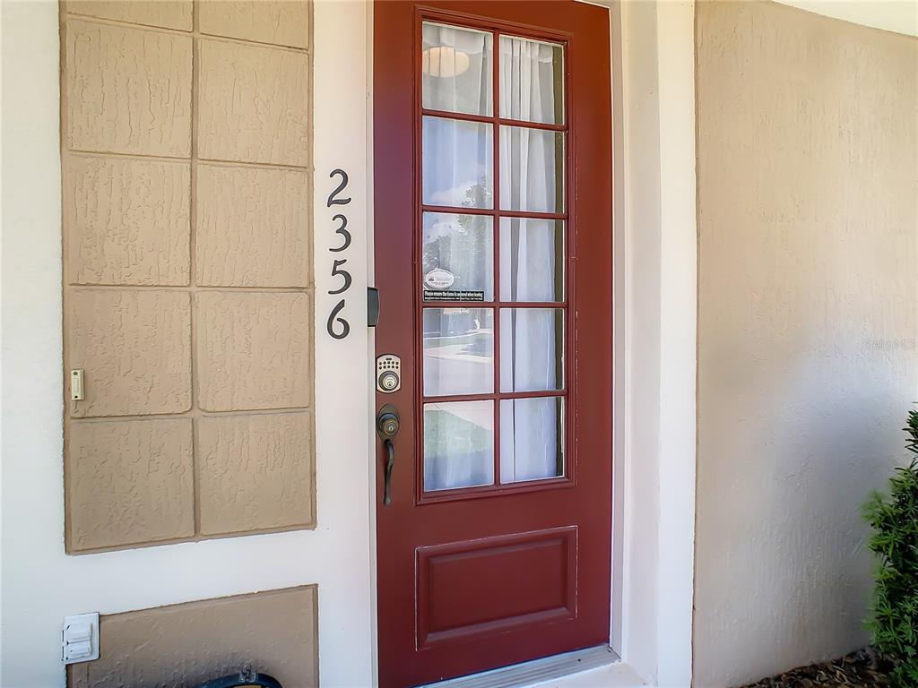 A red front door with glass panes and a keypad lock sits beside a textured wall — 2356 SILVER PALM DRIVE, KISSIMMEE, FL