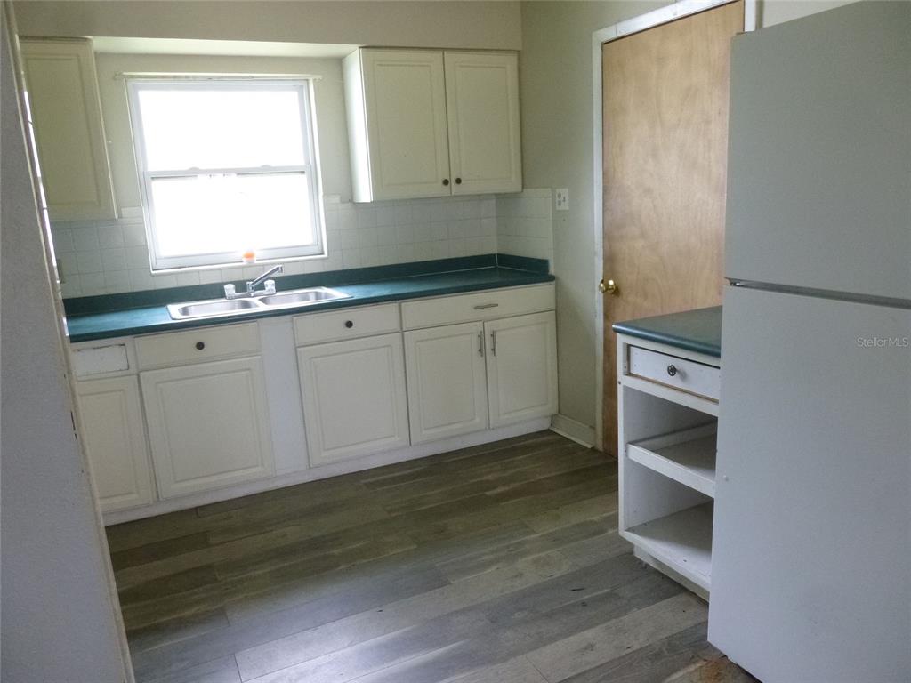 A kitchen features white cabinets, a green countertop, a double sink, and wood-look flooring — 12 HWY 630 W, FROSTPROOF, FL