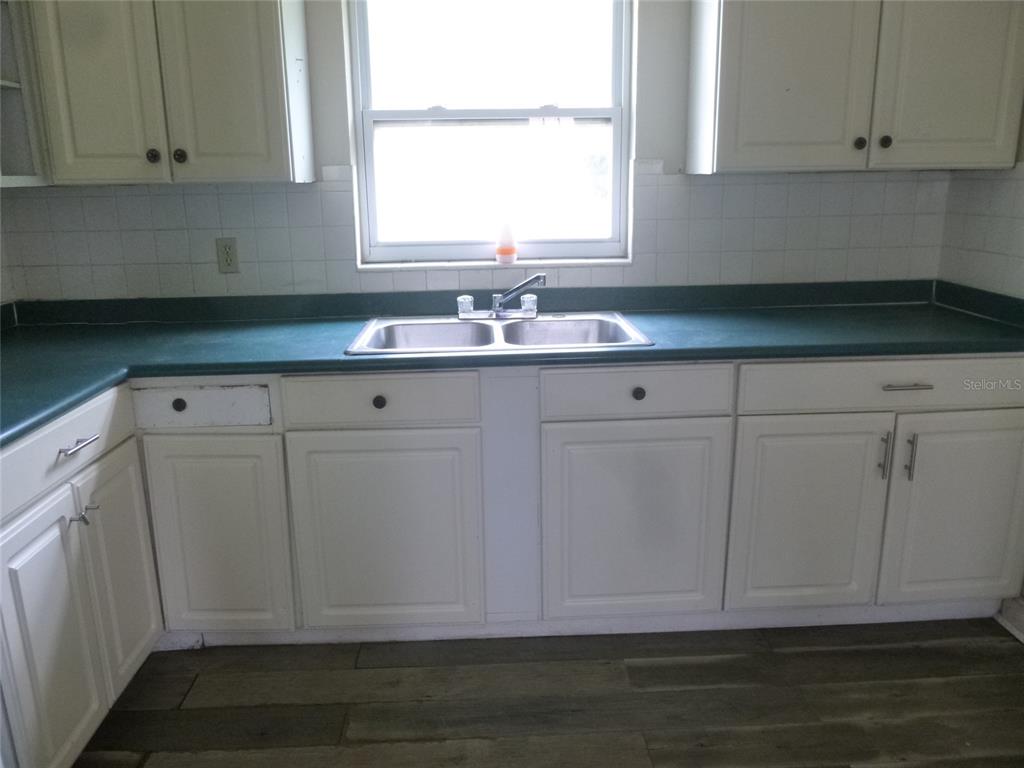A kitchen features white cabinets, a green countertop, a double sink, and wood-look flooring — 12 HWY 630 W, FROSTPROOF, FL