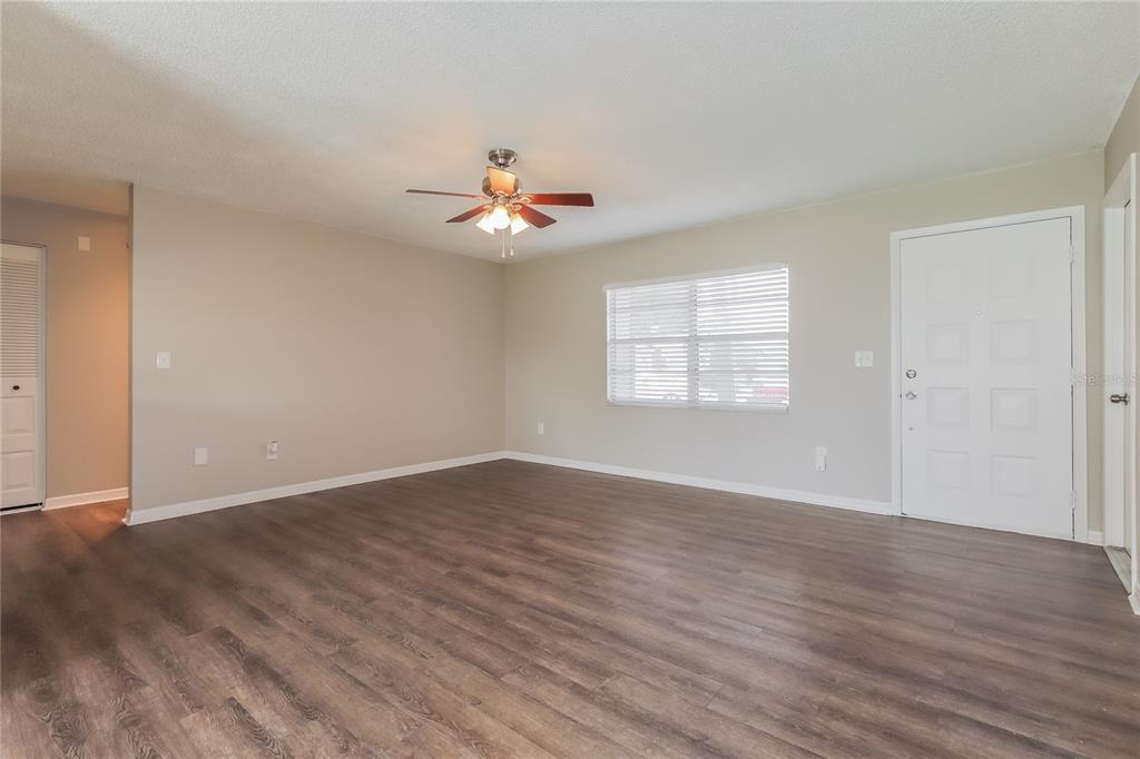 An empty living room with light-colored walls, wood-look flooring, a ceiling fan, and a door — 1002 PINEHAVEN COURT, BRANDON, FL