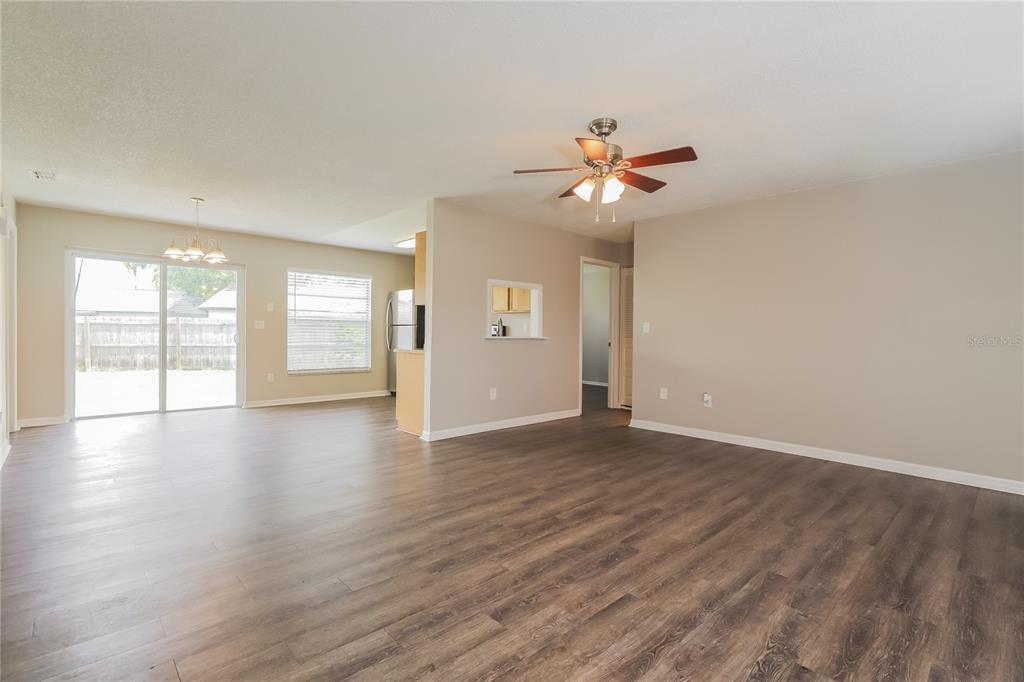 An open-concept living area features wood-look flooring, a ceiling fan, and a kitchen pass-through window — 1002 PINEHAVEN COURT, BRANDON, FL