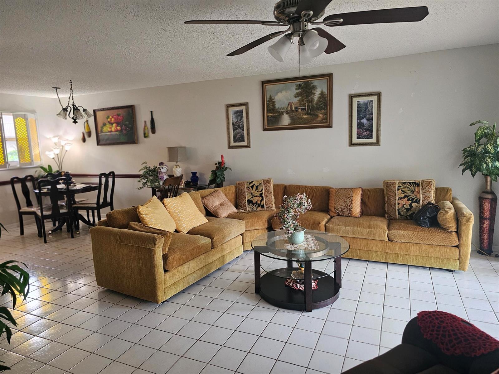 A living room features a large mustard-colored sectional sofa, a glass coffee table, and tile flooring — 721 Lori Dr # 105, Palm Springs FL 33461, PALM SPRINGS, FL