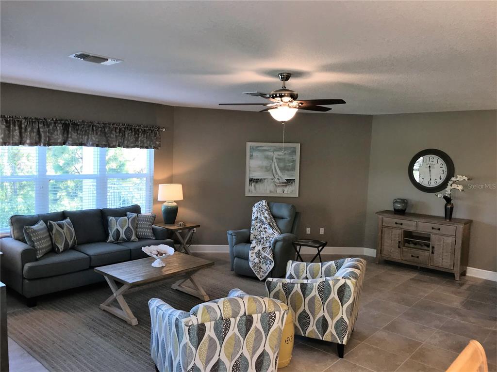 A living room features a gray sofa, two patterned armchairs, a recliner, and a wooden console — 7730 34TH AVENUE W UNIT 101, BRADENTON, FL