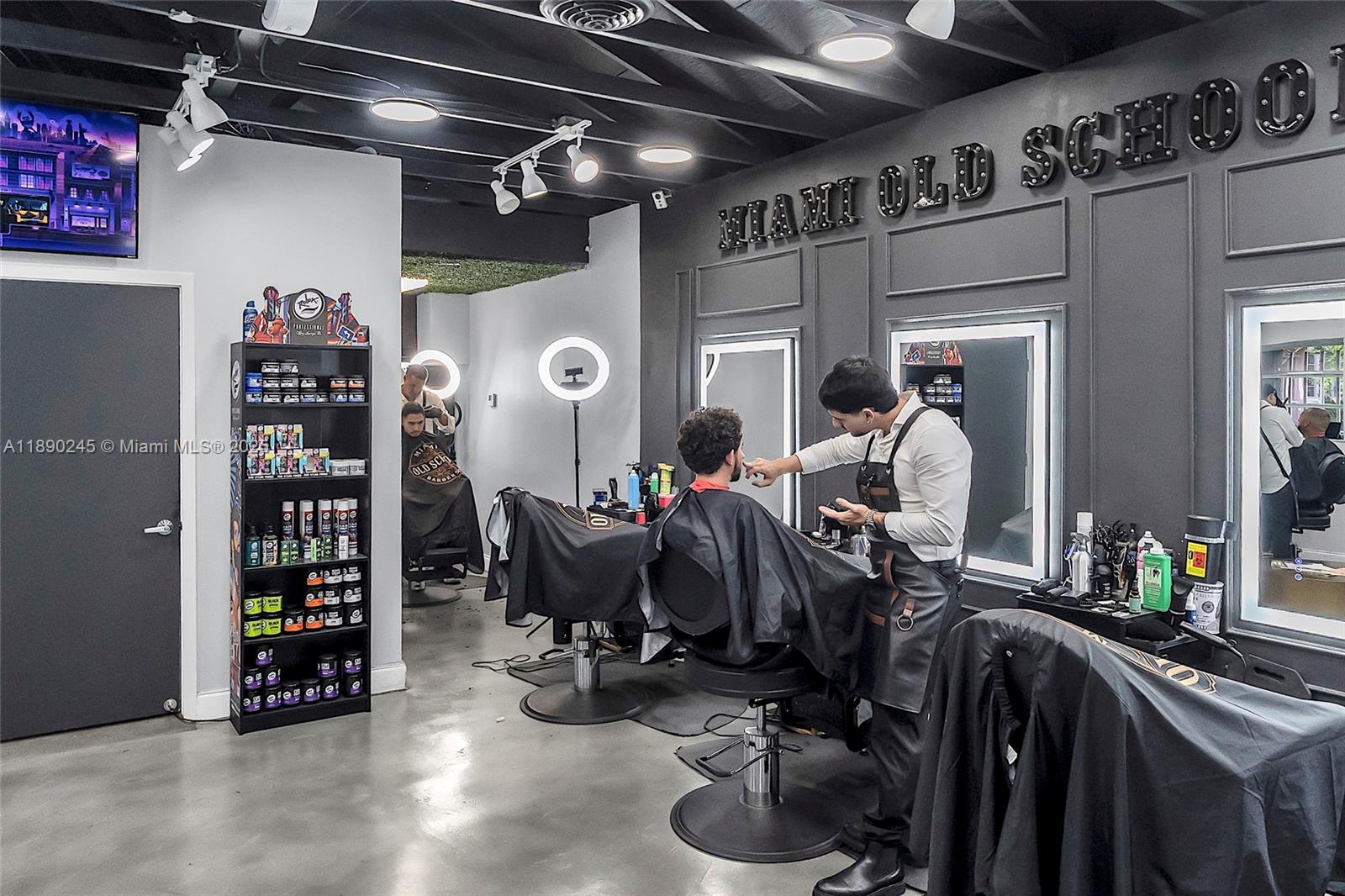 A modern barbershop features black walls, illuminated signage, multiple styling stations, and a product display shelf — 2700 Biscayne Blvd, Miami FL 33137, MIAMI, FL