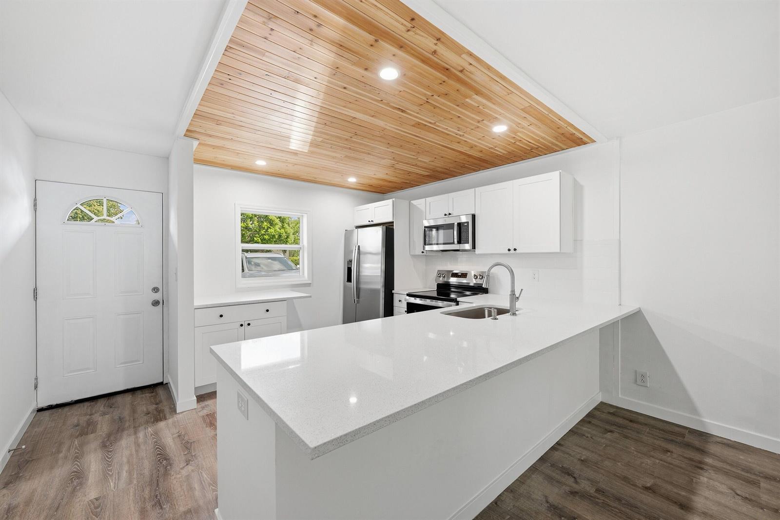 A modern kitchen features white cabinets, quartz countertops, and a wood-paneled ceiling — 330 NE 26th Avenue # 112, Boynton Beach FL 33435, BOYNTON BEACH, FL