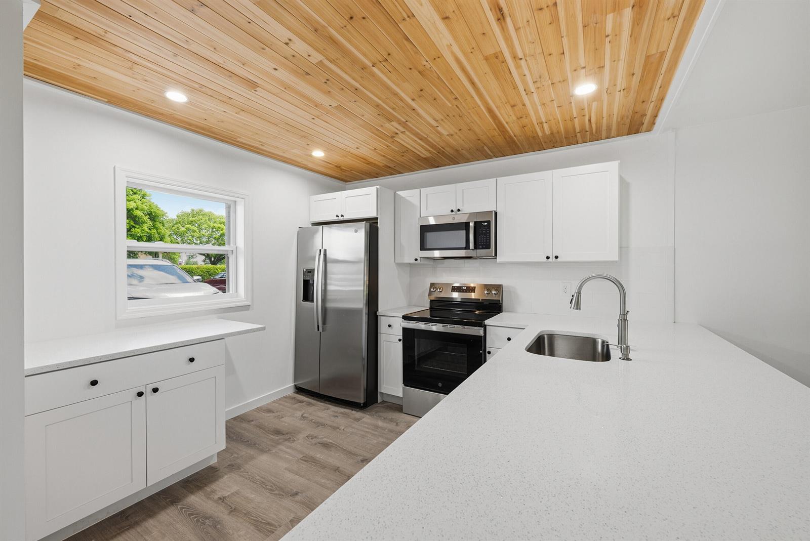 A kitchen features white cabinets, stainless steel appliances, quartz countertops, and a wood-plank ceiling — 330 NE 26th Avenue # 112, Boynton Beach FL 33435, BOYNTON BEACH, FL