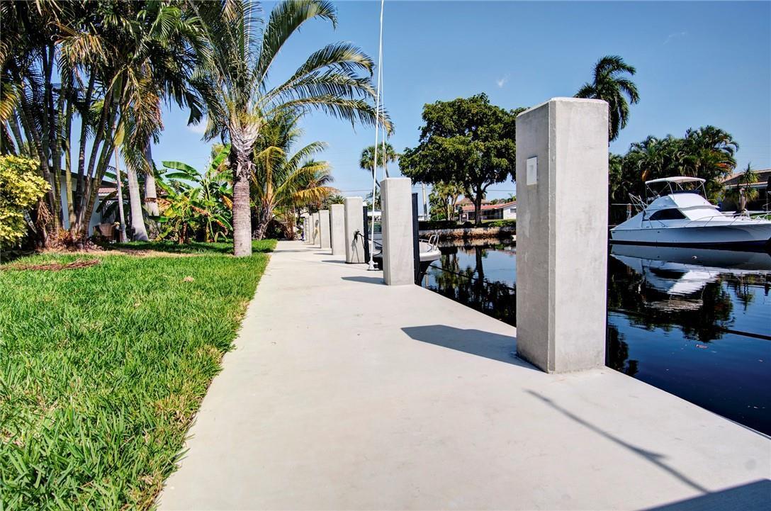 A concrete dock runs alongside a canal with palm trees and a docked boat — 3860 NE 23rd Avenue, Lighthouse Point FL 33064, LIGHTHOUSE POINT, FL