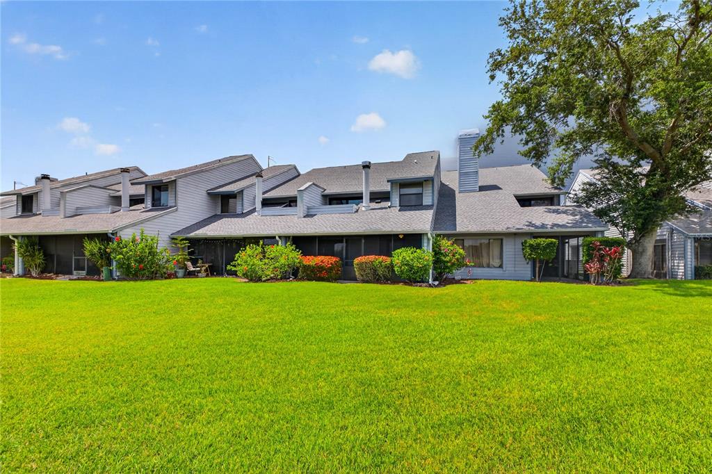 The rear exterior of a multi-unit townhouse complex features screened-in patios and a large lawn — 9050 PARK BOULEVARD UNIT 7, SEMINOLE, FL