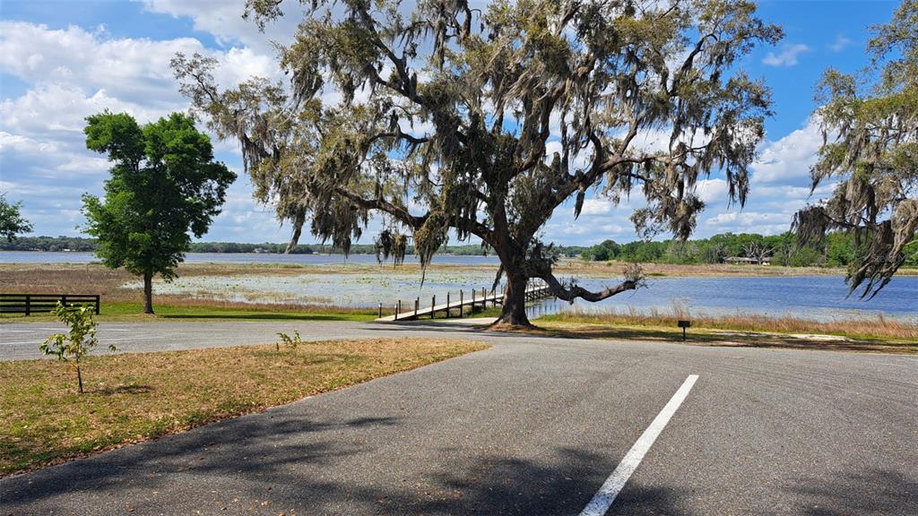 A paved parking area overlooks a lake with a wooden dock and large mossy trees — 00 SE 101ST CT ROAD, BELLEVIEW, FL