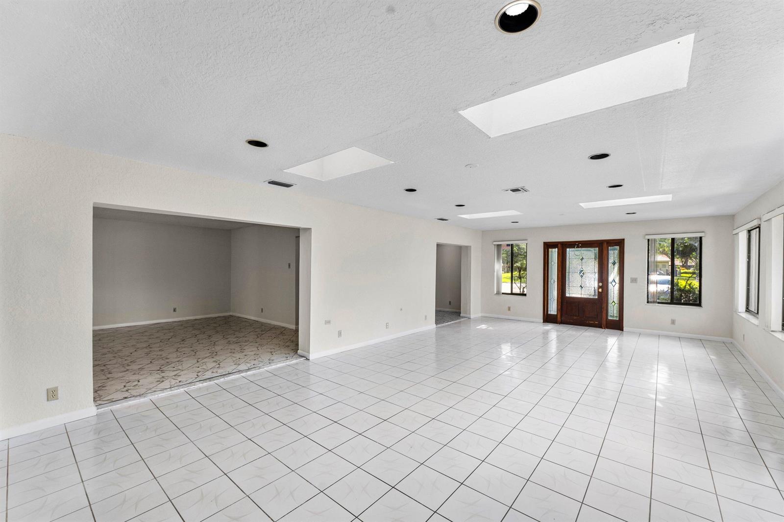A spacious room with white tile flooring, recessed lighting, skylights, and a wooden front door — 900 NW 30th Avenue # D, Delray Beach FL 33445, DELRAY BEACH, FL